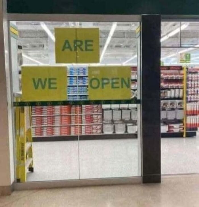 Confusing store sign with words arranged to read Are We Open across glass doors inside a supermarket aisle.