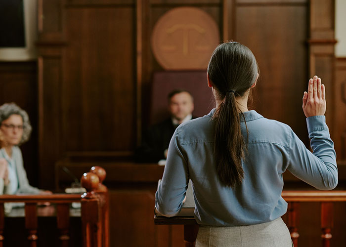 Woman taking oath in court during award winning act case, with judge and witness in the background. Woman taking oath in court during award winning act case, with judge and witness in the background.