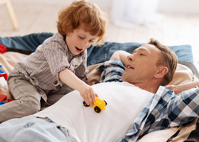 Father lying on bed playing with his young son holding a yellow toy car, capturing family moments and bonding time. Father lying on bed playing with his young son holding a yellow toy car, capturing family moments and bonding time.