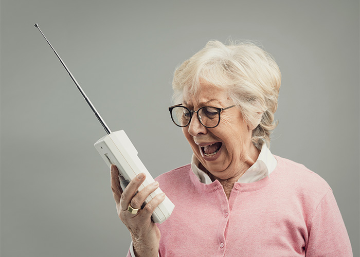 Elderly woman in pink sweater angrily shouting into a vintage mobile phone, representing Gen Z male Karen concept.