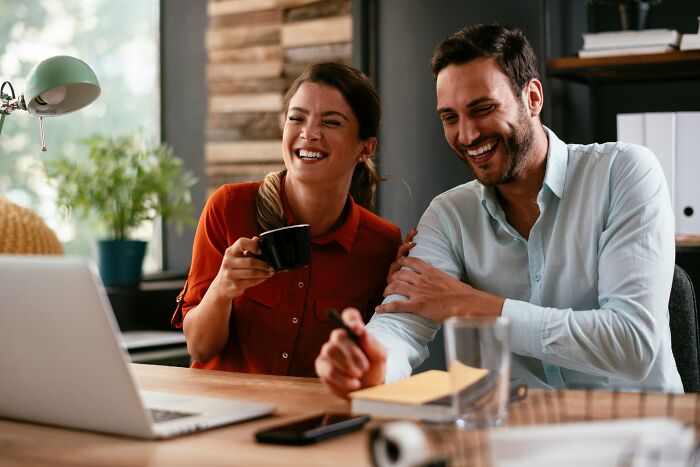 Two coworkers laughing together during a casual office meeting, highlighting the contrast of worst coworker stories.
