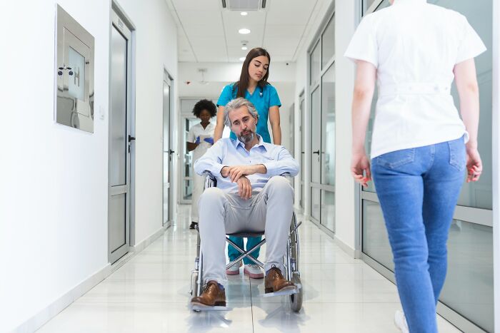 Hospital workers pushing a tired male patient in a wheelchair down a bright hospital corridor
