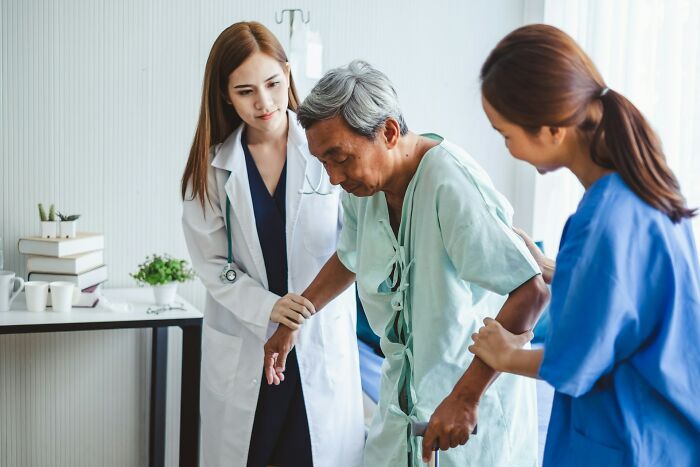 Hospital Workers help elderly male patient with cane, doctor and nurse supporting him in a hospital room