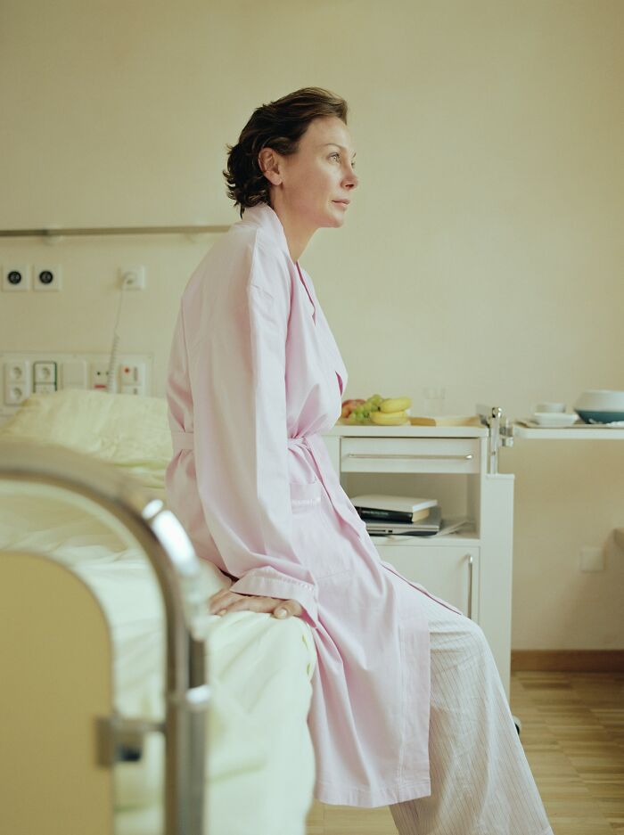 Woman in a hospital gown sitting on bed, reflecting on a really bad prognosis and unexplainable medical events.