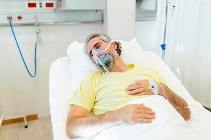 Male patient lying in hospital bed with oxygen mask, illustrating examples of a doctor doing something unethical with a patient.