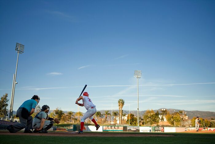 High school baseball game at sunset with batter, catcher, and umpire, highlighting moments beyond just education.