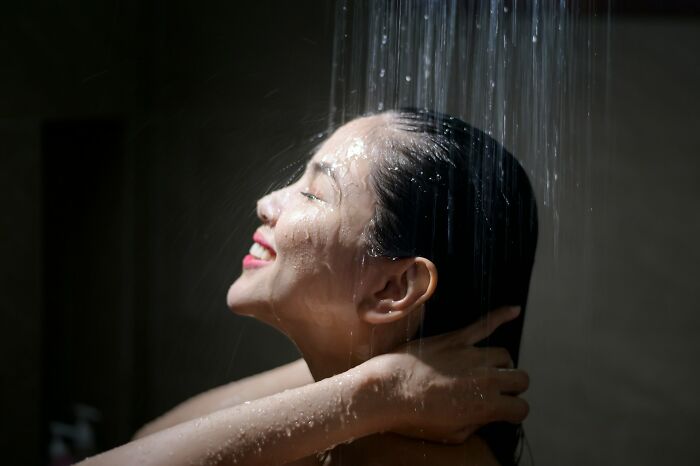 Woman smiling under shower water, highlighting daily dangers you might not realize you're exposing yourself to.