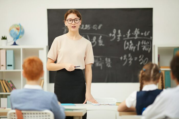 Teacher standing in front of a classroom teaching math, illustrating weirdest teacher behavior witnessed in class by students.