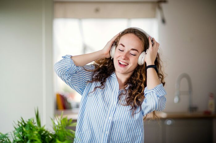 Young woman in kitchen wearing headphones, smiling and dancing, creepiest displays of intelligence