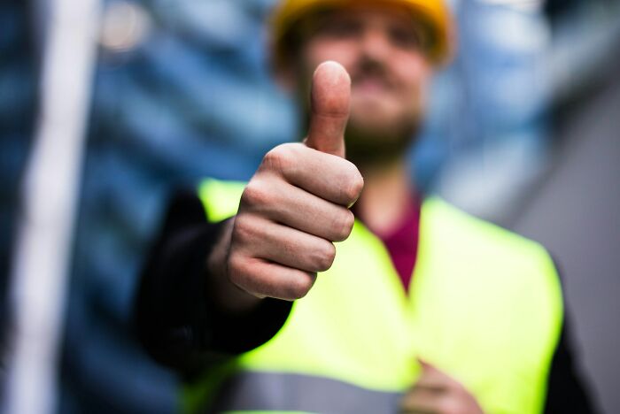 Man in safety vest and helmet giving thumbs up, an example of gestures normal in America but offensive elsewhere.
