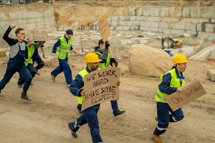 Construction workers in Europe wearing helmets and vests holding protest signs during a labor strike demonstration.