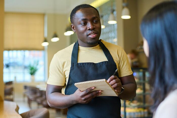 Waiter wearing apron taking order from customer in a casual restaurant, illustrating things normal in America but offensive elsewhere.