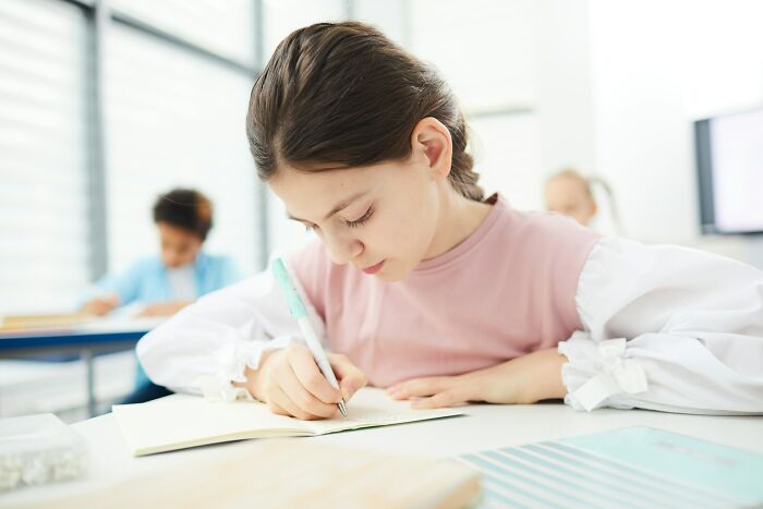 Young student focused on writing in a notebook during class, illustrating weird teacher behavior witnessed in school settings.