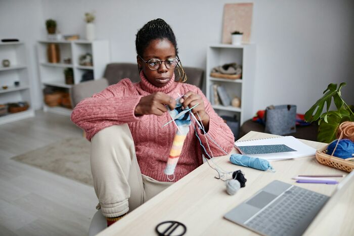 Woman knitting at home in a cozy sweater, practicing safety and comfort habits while living alone. Woman knitting at home in a cozy sweater, practicing safety and comfort habits while living alone.