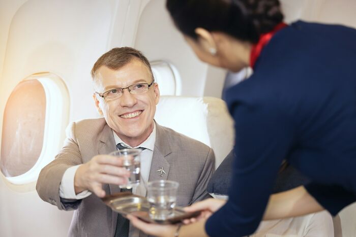 A businessman smiling while receiving a drink from a flight attendant during an in-flight service on an airplane.