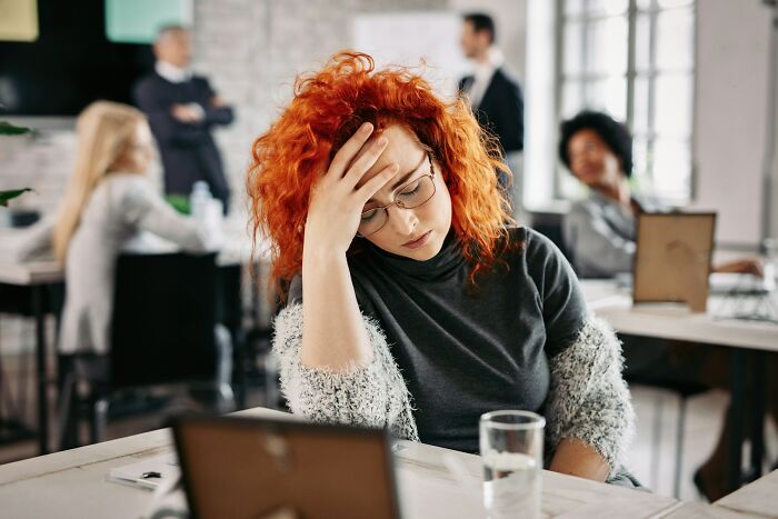 Woman with red hair looking stressed at work, illustrating common adult goals that many find overrated in daily life.