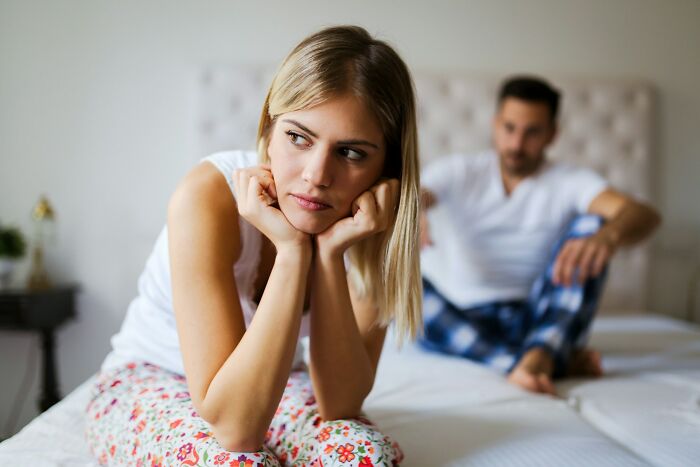 Young woman looking upset on bed while man in background appears distant, representing wedding moments that didn’t last.