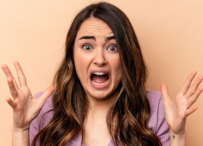 Young woman with long hair looking shocked and raising hands, expressing suspicion and disbelief about cheating with roommate.