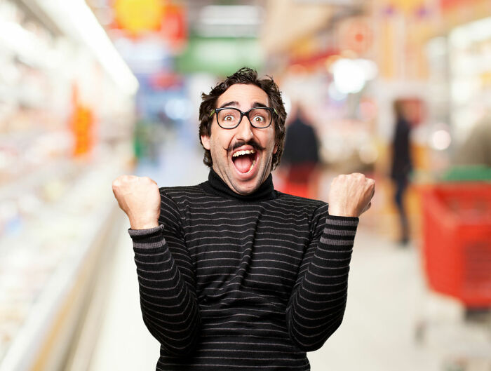 Man with glasses and mustache in a striped sweater showing excitement while food shopping, appearing highly triggered and coping.