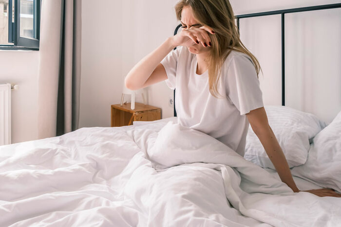 Woman sitting on bed, wiping her eyes, expressing distress related to food shopping triggering emotional response. Woman sitting on bed, wiping her eyes, expressing distress related to food shopping triggering emotional response.