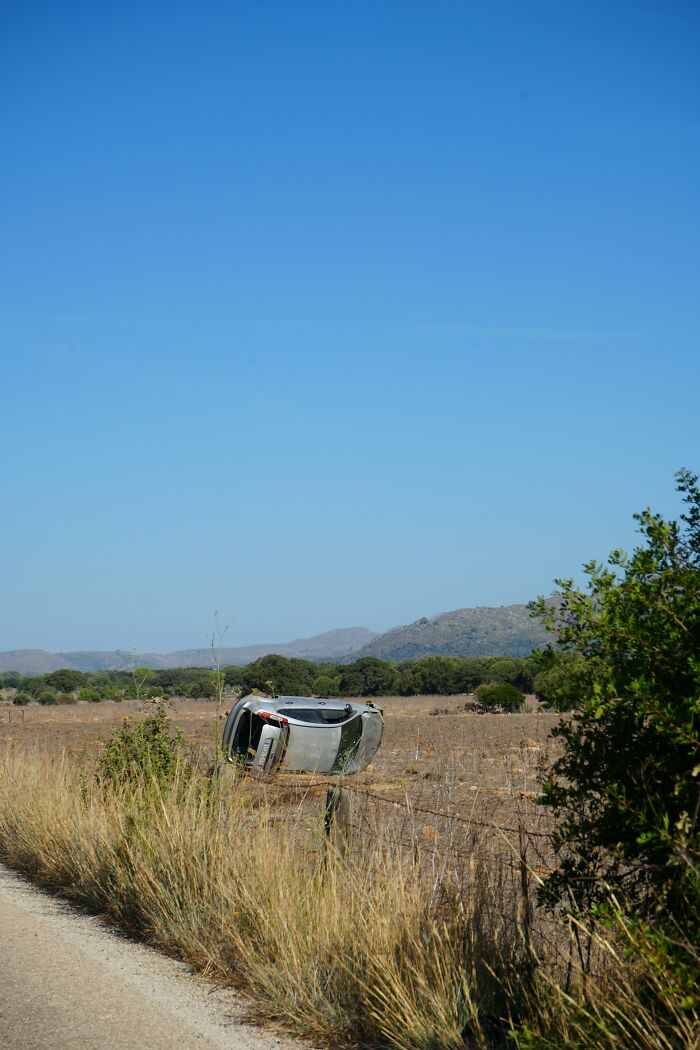 Overturned car in dry field under clear blue sky, evoking surreal rained frogs anecdote.