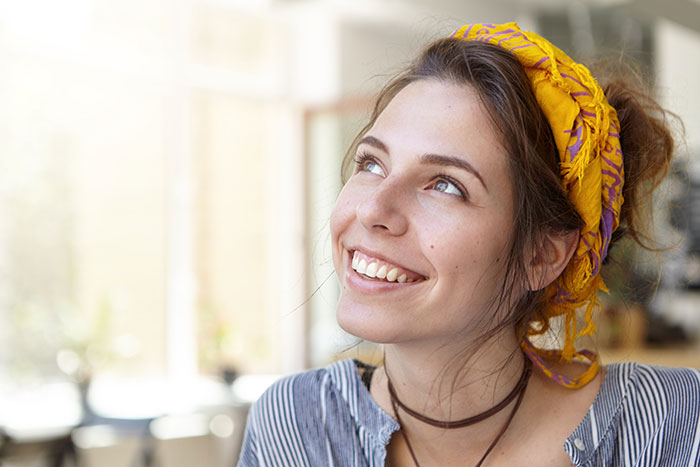 Young gifted woman wearing a yellow headscarf, smiling and looking up, reflecting potential and future success.