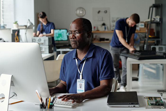 Middle-aged man focused on computer work in a modern office with colleagues, showcasing gifted kids potential theme.