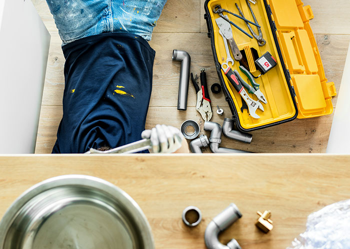 Man fixing plumbing pipes on the floor with tools and a toolbox, illustrating feelings of emasculation in relationships. Man fixing plumbing pipes on the floor with tools and a toolbox, illustrating feelings of emasculation in relationships.