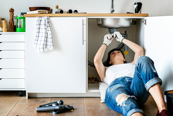 Woman fixing plumbing under kitchen sink, wearing gloves and casual clothes, showing independence and strength. Woman fixing plumbing under kitchen sink, wearing gloves and casual clothes, showing independence and strength.