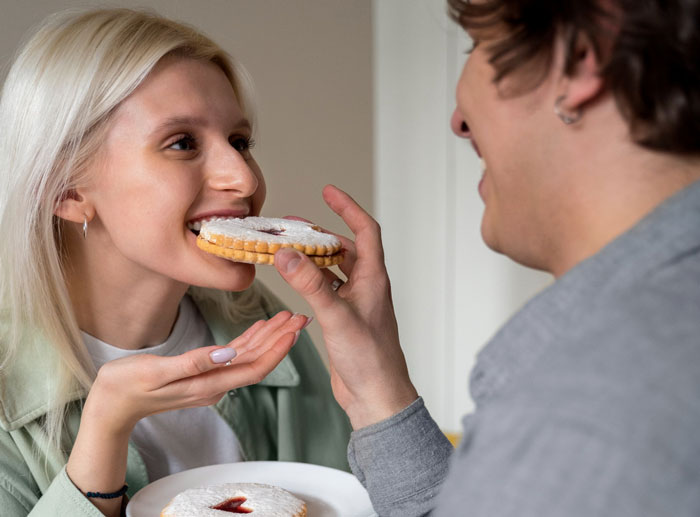 Young woman and her male bestie planning a cruel prank by feeding a cookie to humiliate her boyfriend on his birthday.