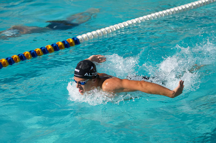 Swimmer boyfriend wearing cap and goggles swimming butterfly stroke in pool, related to woman demands keyword scenario. Swimmer boyfriend wearing cap and goggles swimming butterfly stroke in pool, related to woman demands keyword scenario.