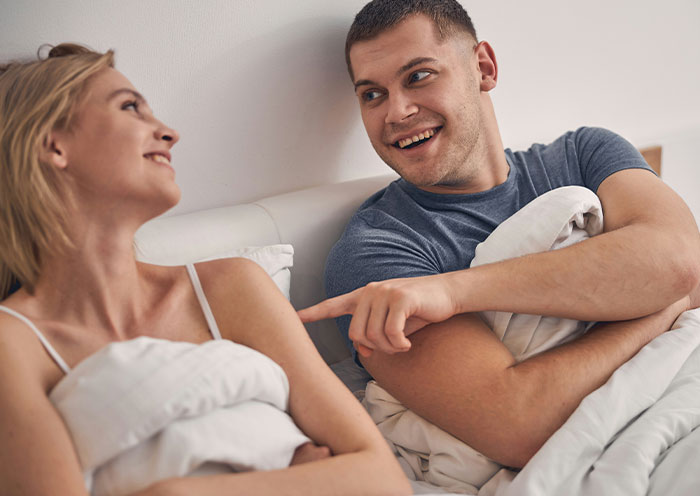 Couple in bed having a playful conversation, highlighting woman demanding swimmer boyfriend look like her friend’s partner. Couple in bed having a playful conversation, highlighting woman demanding swimmer boyfriend look like her friend’s partner.