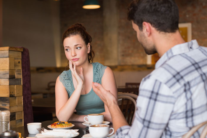 Man horrified as girlfriend appears upset during a tense conversation over food at a cafe table. Man horrified as girlfriend appears upset during a tense conversation over food at a cafe table.