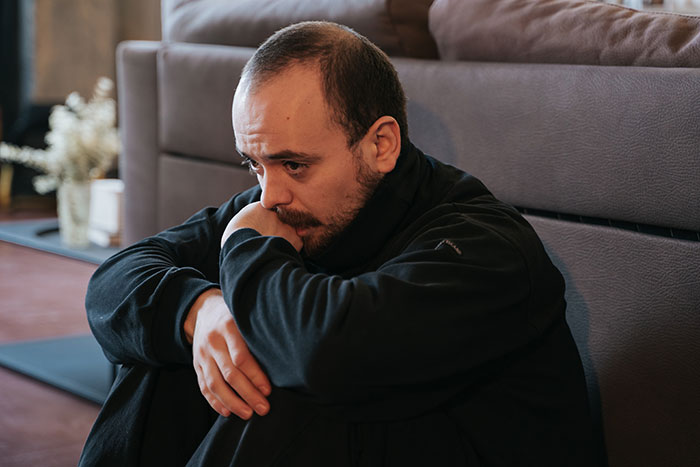 Man sitting on floor looking furious and upset after family refuses to include him in girl days activities. Man sitting on floor looking furious and upset after family refuses to include him in girl days activities.