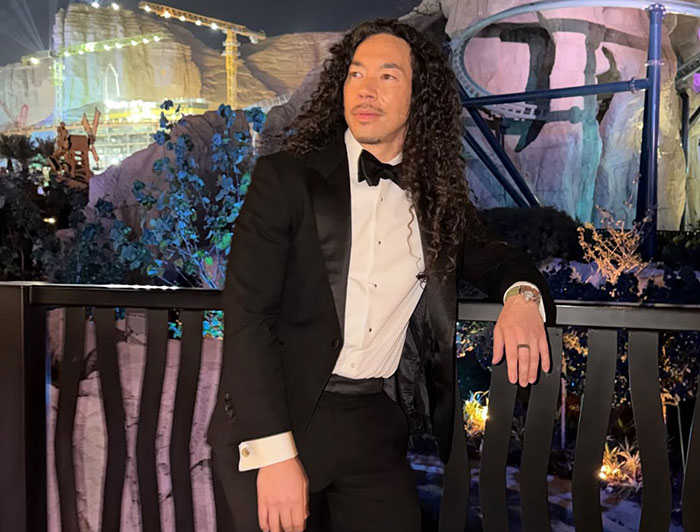 GlamBOT King in a black tuxedo posing outdoors at night after viral interaction at the Golden Globes event.