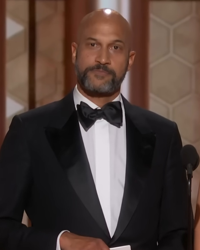 Actor in a tuxedo speaking at 2026 Golden Globes amid chaos with stars leaving early and smoking despite ban.