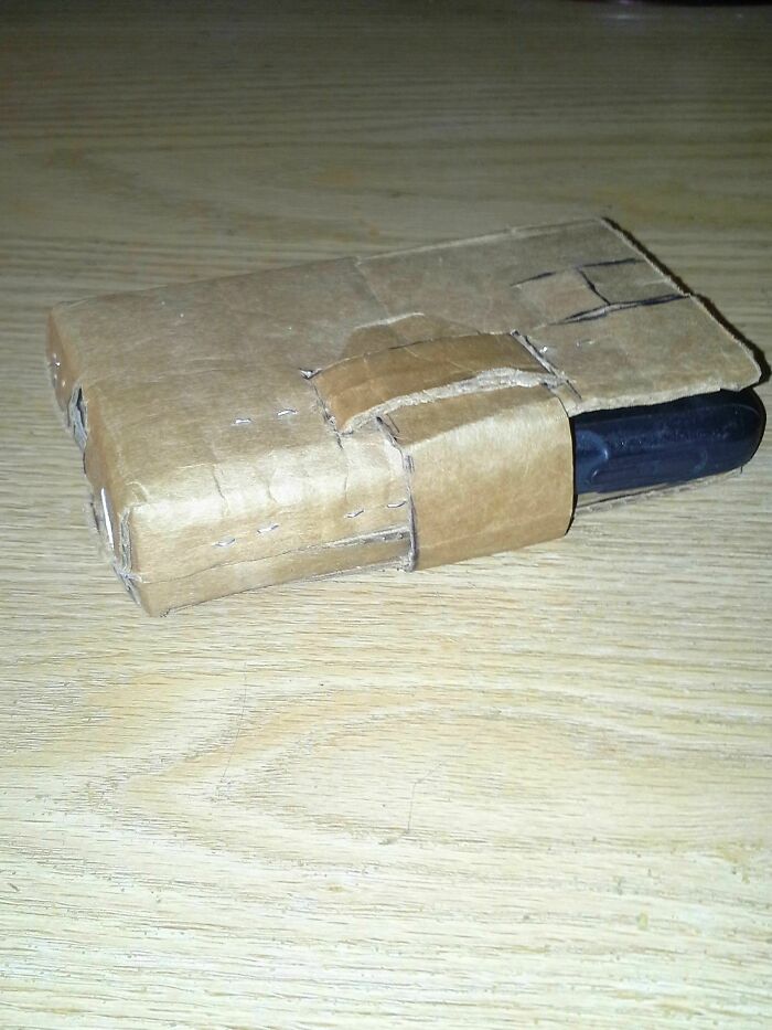 Phone wrapped in cardboard as a failed DIY phone case placed on a wooden surface showing poor craftsmanship.