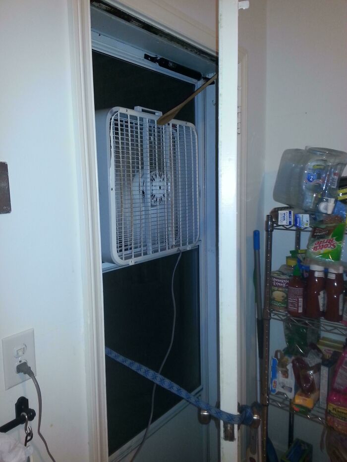 Box fan awkwardly installed in window with a wooden spoon and rope, a clear example of DIY fail and poor craftsmanship.