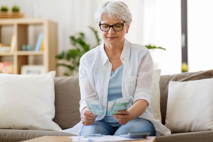 Older woman counting money at home, illustrating a greedy MIL wedding gift concept in a casual living room setting.