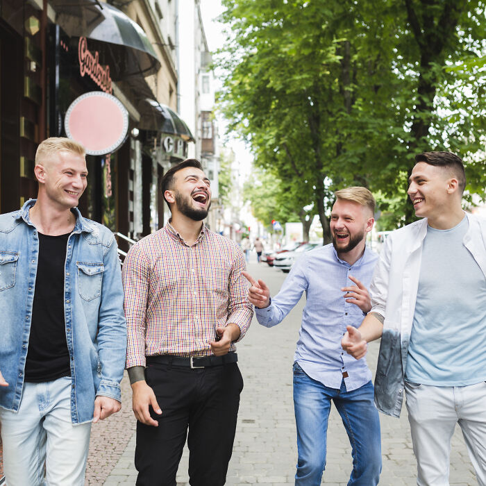 Four men laughing and walking on a city street while people share wildest ways found out cheating experiences.