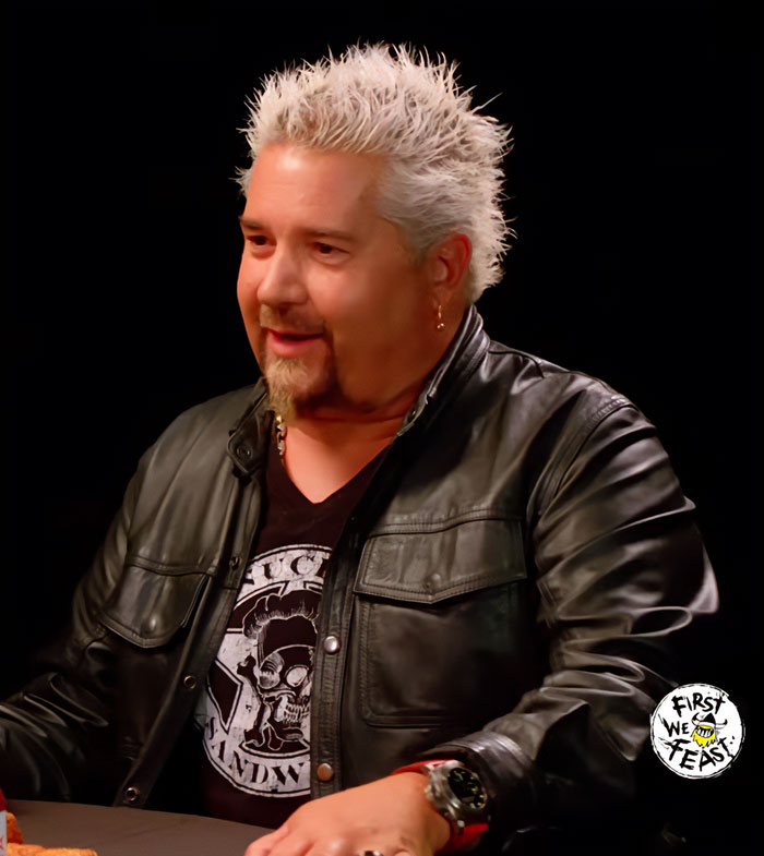 Guy Fieri with spiky blonde hair and leather jacket, discussing his 58th birthday glow-up on a podcast.
