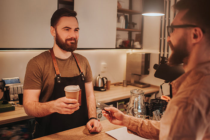 Barista handing a coffee cup to a smiling customer in a cozy coffee shop during a morning rush. Barista handing a coffee cup to a smiling customer in a cozy coffee shop during a morning rush.