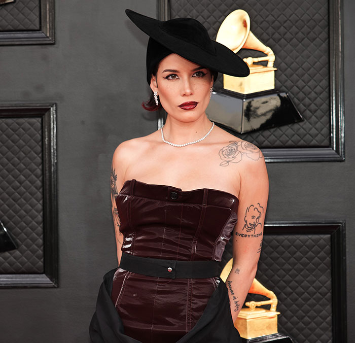 Woman in a dark strapless dress and wide-brimmed black hat posing at Grammy awards discussing Grammy snubs and fan psychology.