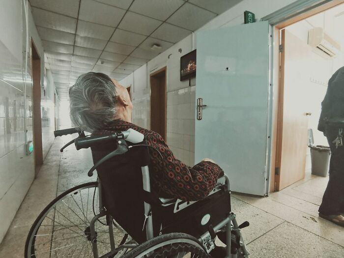 Elderly patient in wheelchair in dim hospital corridor, highlighting unethical doctor behavior with patient concerns.