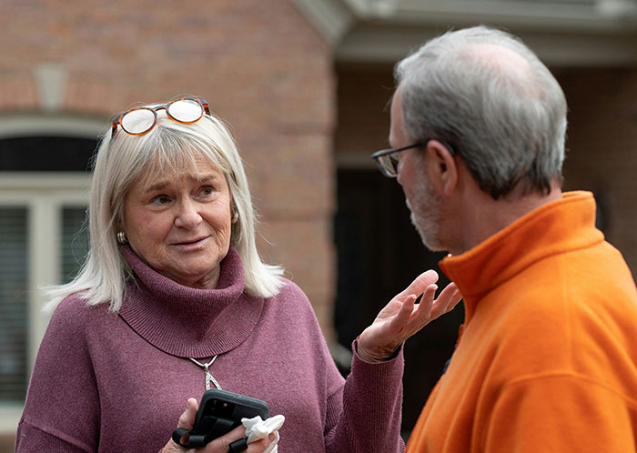 Older woman speaking with a man outside a house, representing an HOA president involved in a power-trip harassment dispute.