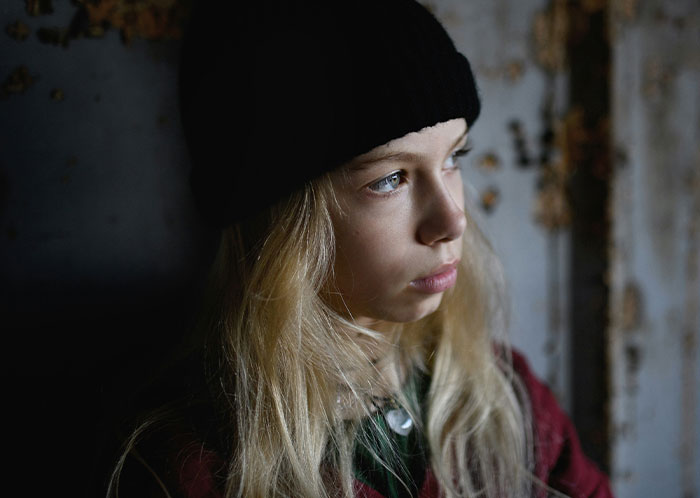 Young person with a somber expression wearing a black beanie, reflecting the harsh realities of homeless experiences.