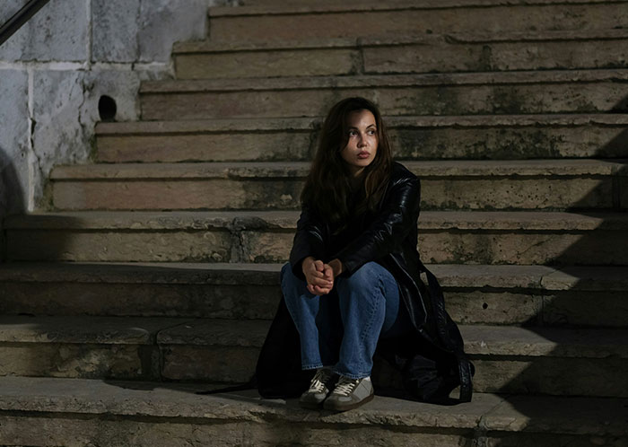 Woman sitting alone on worn stone steps at night, depicting the harsh reality of homeless people’s horrifying experiences.