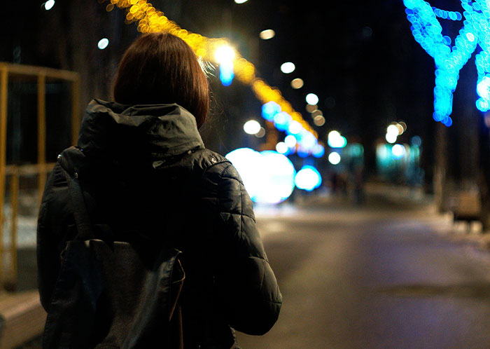 Person in a dark jacket walking alone at night on a blurred city street, symbolizing homeless people’s horrifying experiences.