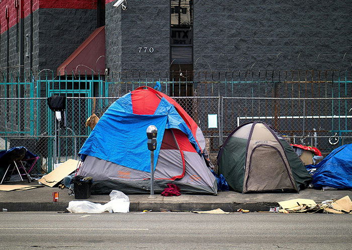 Tents set up on city sidewalk depicting homeless people and their harsh living conditions on urban streets.