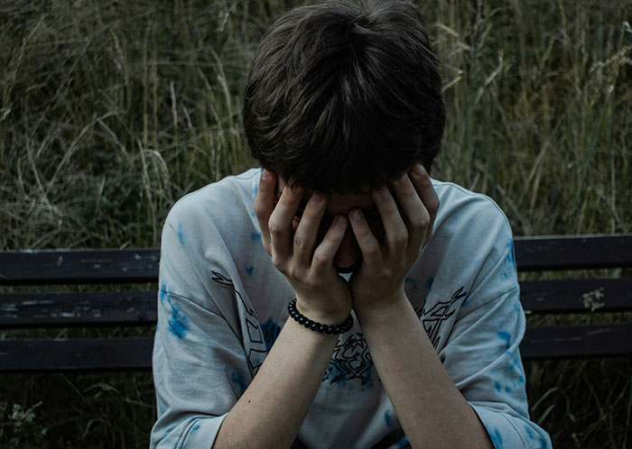Young man sitting on a bench outdoors covering his face, reflecting the struggles of homeless people’s horrifying experiences.